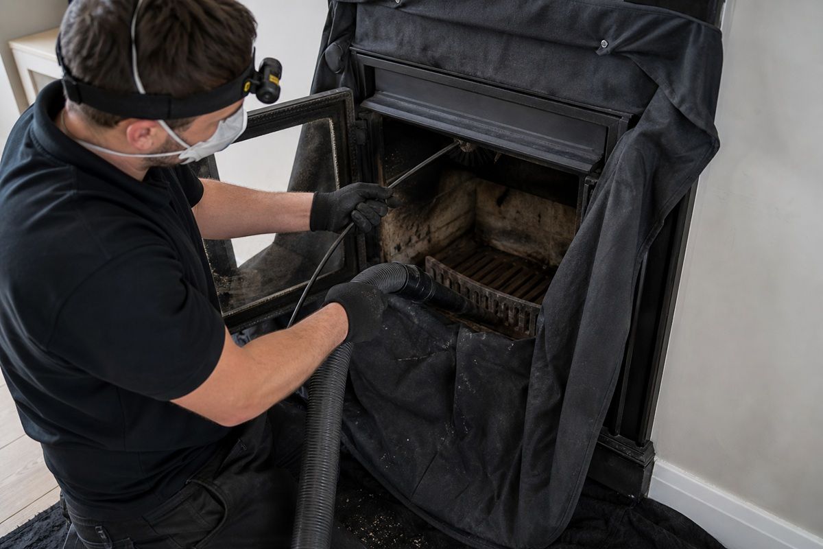 Chimney professional cleaning a fireplace with dust-control equipment