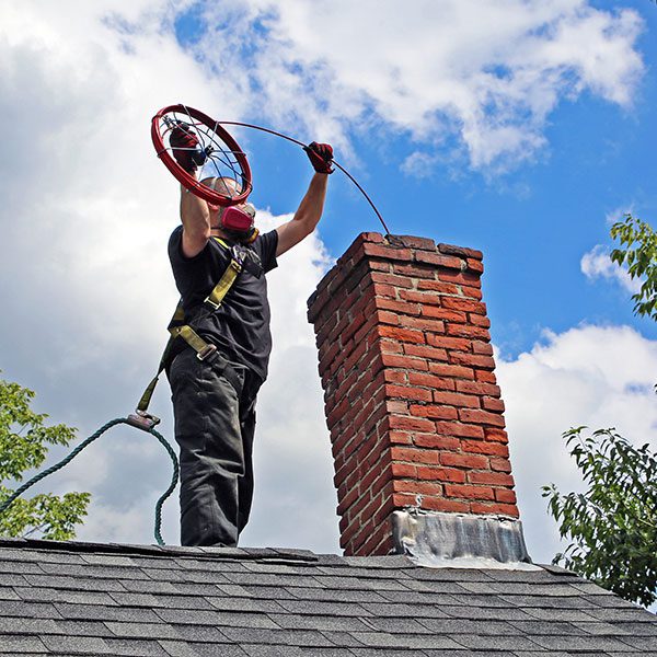 Chimney technician guiding rotary cleaning equipment into a brick chimney