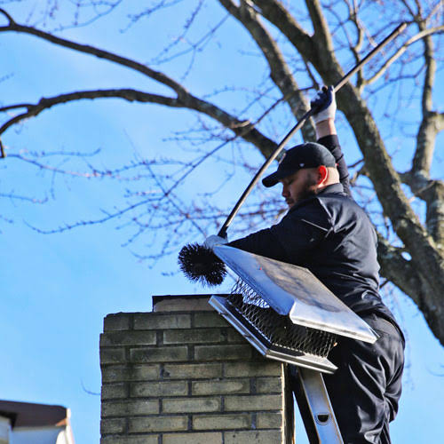 Chimney technician working from a ladder beside a metal chimney cap
