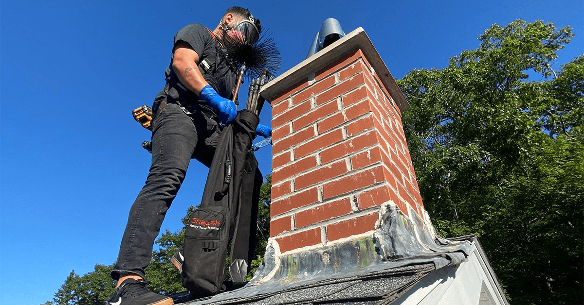 Chimney professional evaluating a brick chimney crown and flashing on a roof