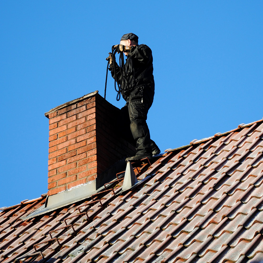 Chimney professional lowering service equipment into a rooftop brick chimney