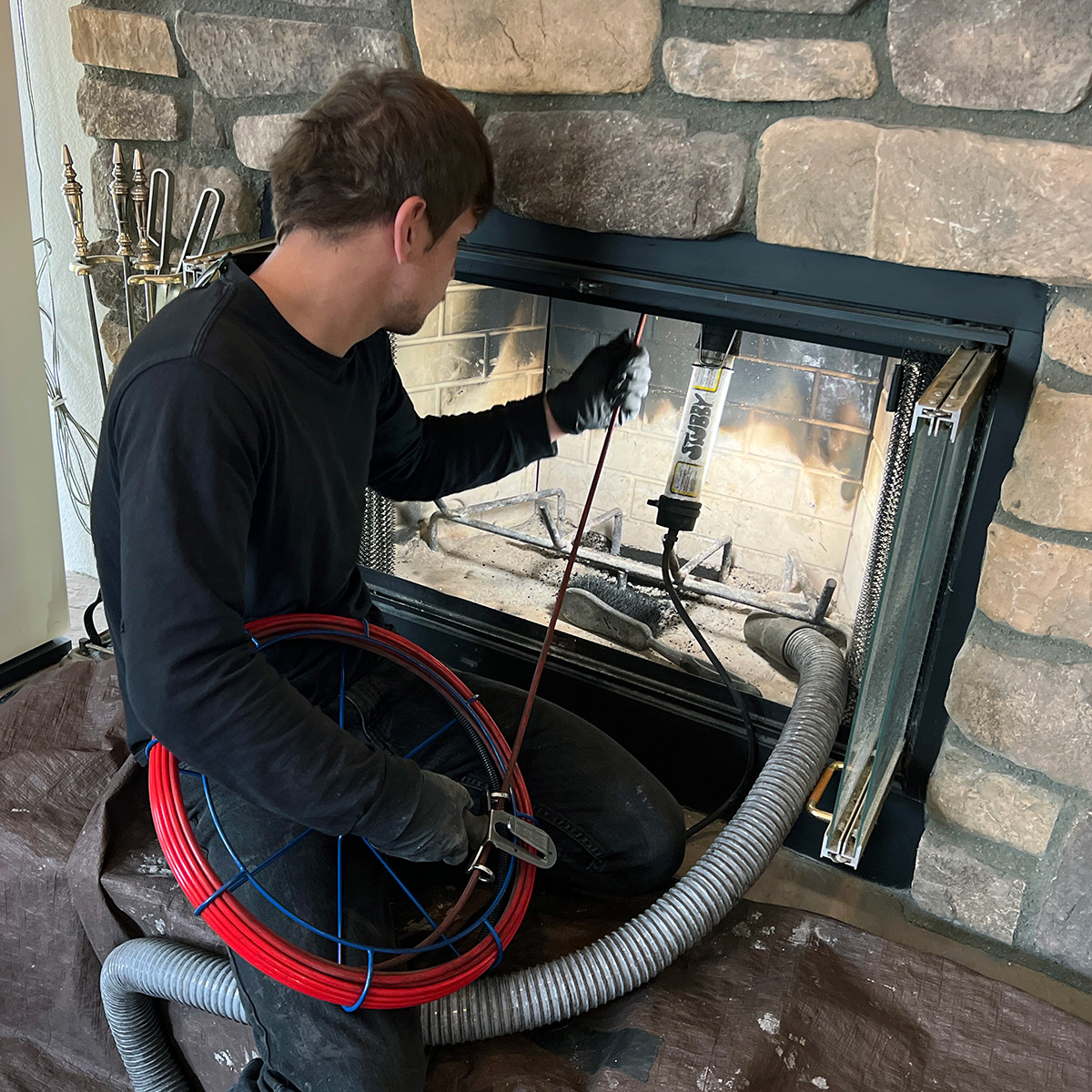 Technician using fireplace service equipment beside a stone hearth
